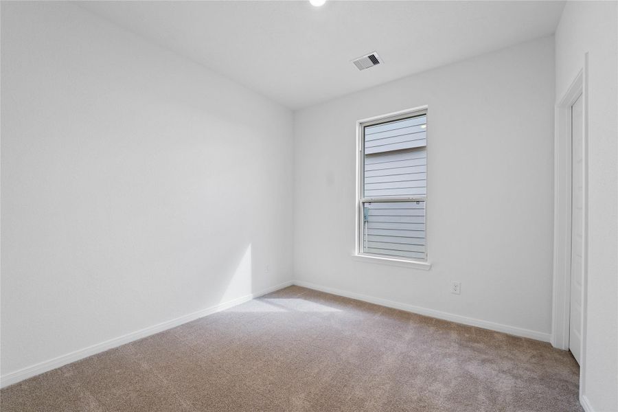 One of the three secondary bedrooms, pictured here, offers comfort and style with plush carpeting, neutral paint tones, recessed lighting, a large window, and a walk-in closet.