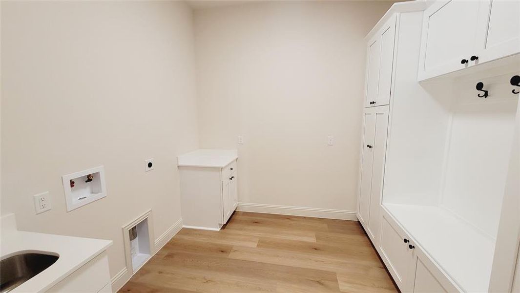 Dedicated utility space featuring extensive built-in white cabinetry, wood-finish flooring, and light-toned walls