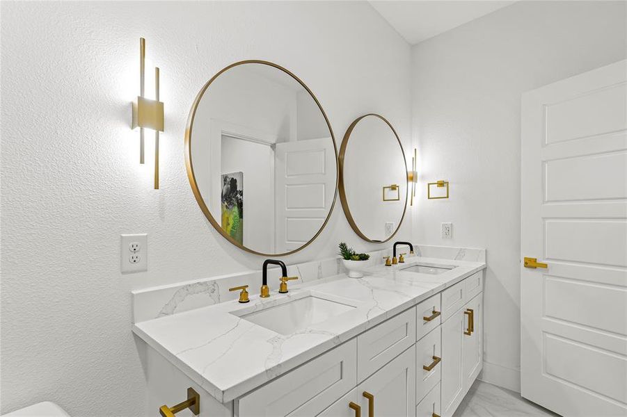 Bathroom with double vanity, a textured wall, and light marble finish flooring