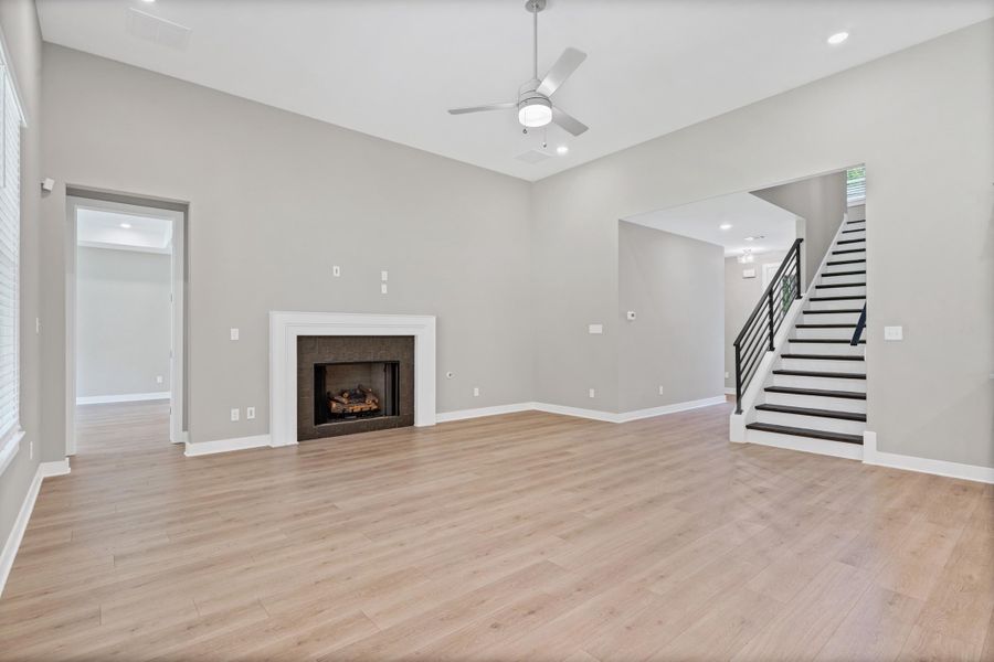 Spacious living area featuring high vaulted ceilings, light wood-finish flooring, and a fireplace with a white mantel and dark stone surround Spacious living area featuring high vaulted ceilings, light wood-finish flooring, and a fireplace with a white mantel and dark stone surround