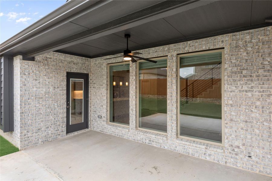 Covered back patio with ceiling fan, large windows, and glass door on brick exterior wall