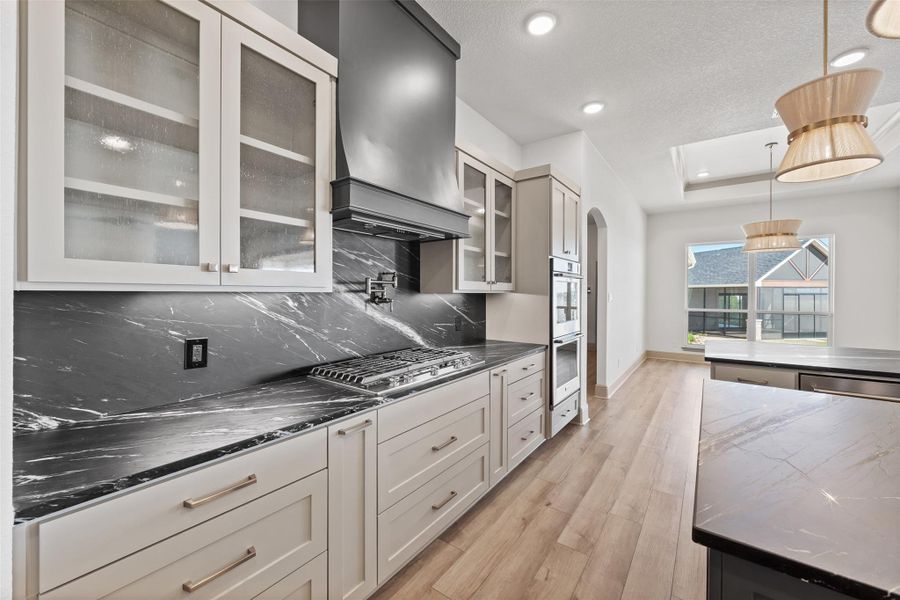 Kitchen with a raised ceiling, light wood-style floors, arched walkways, stainless steel appliances, and wall chimney exhaust hood