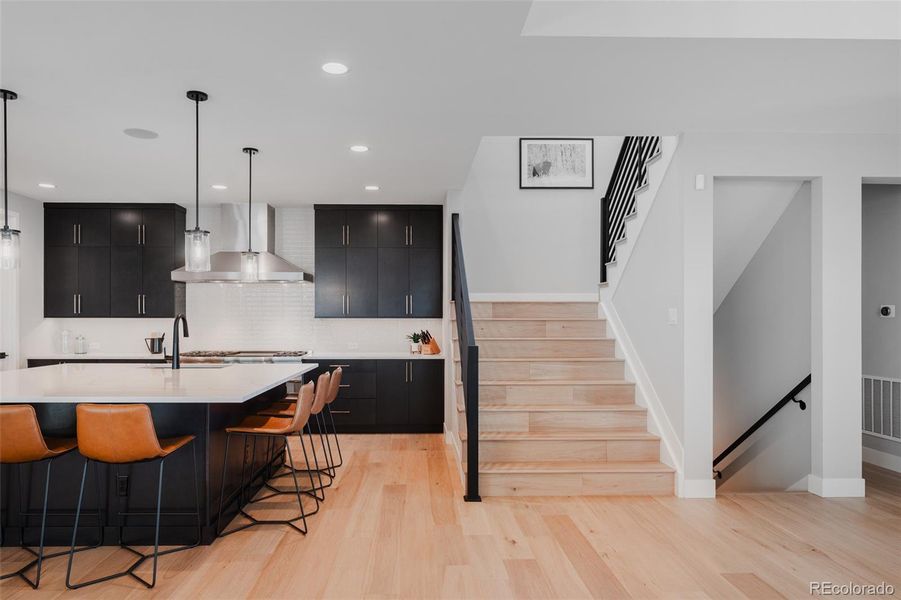 A wide staircase laid with natural white oak and framed by sleek black railings serves as a stunning architectural feature, gracefully leading to both the upper and lower levels.