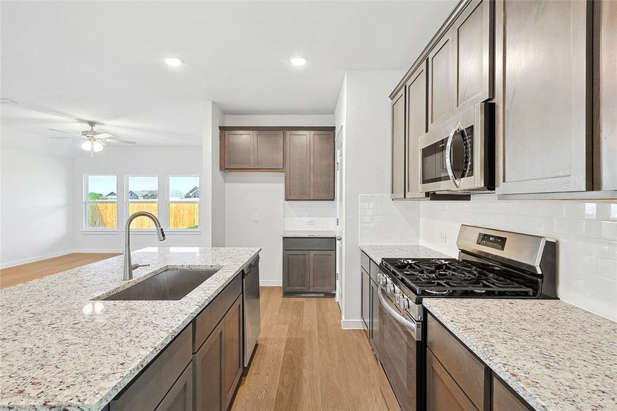 Kitchen with appliances with stainless steel finishes, backsplash, sink, and light hardwood / wood-style flooring