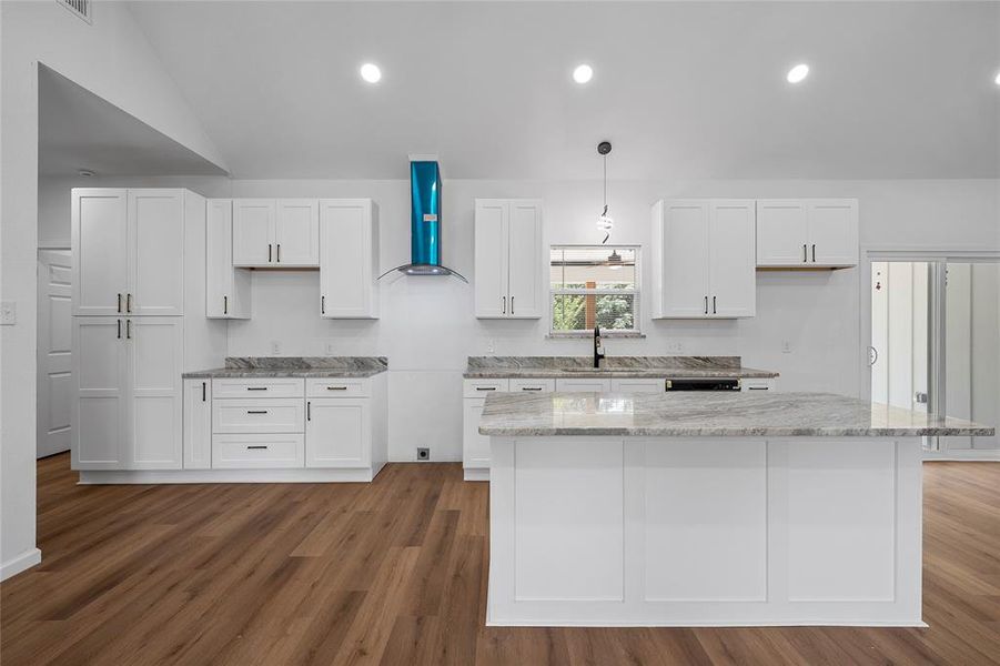 Modern kitchen featuring a central island with an extended counter, white shaker-style cabinetry, dark hardware, light-toned countertops, and wood-finish flooring Modern kitchen featuring a central island with an extended counter, white shaker-style cabinetry, dark hardware, light-toned countertops, and wood-finish flooring