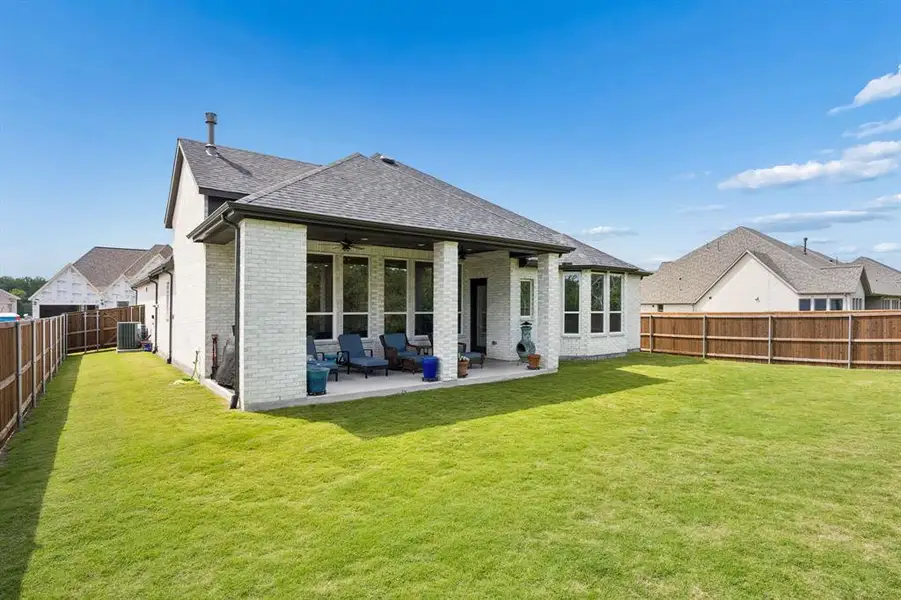 Expansive backyard featuring a covered patio, a full privacy fence, a brick exterior, and multiple windows Expansive backyard featuring a covered patio, a full privacy fence, a brick exterior, and multiple windows