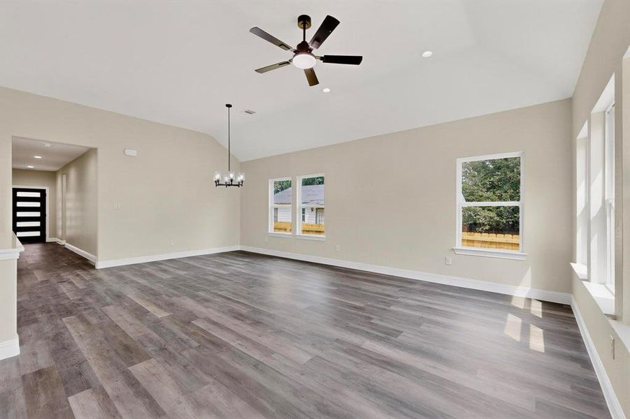 Unfurnished living room featuring recessed lighting, light wood-style flooring, ceiling fan, lofted ceiling, and a chandelier Unfurnished living room featuring recessed lighting, light wood-style flooring, ceiling fan, lofted ceiling, and a chandelier