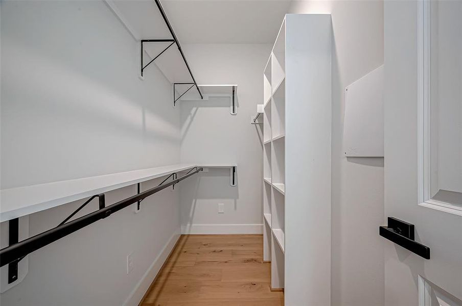 Spacious walk-in closet with ample shelving and hanging space, featuring light wood flooring and a modern, clean design.