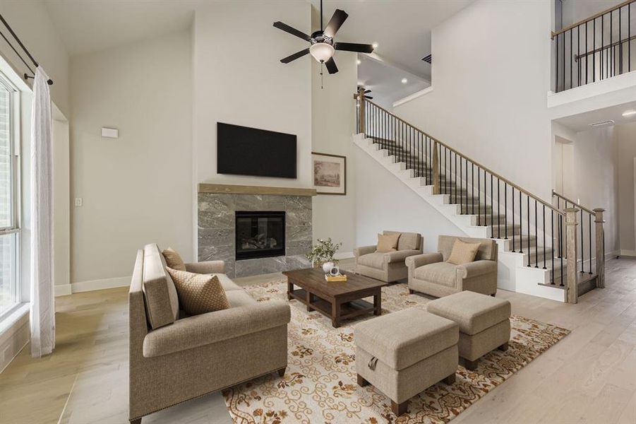 Virtually staged photo - Living room with a high end fireplace, light wood-style flooring, a high ceiling, and ceiling fan