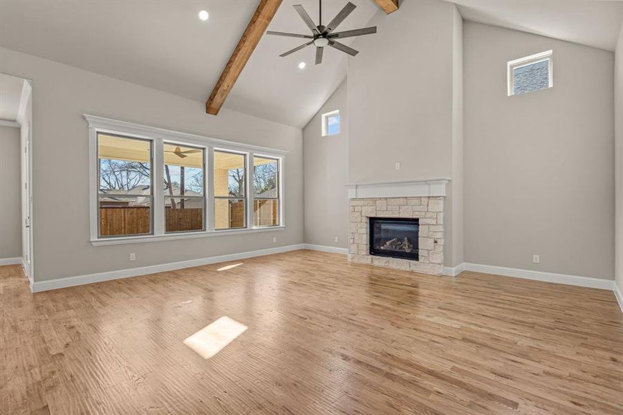 Unfurnished living room featuring high vaulted ceiling, beamed ceiling, ceiling fan, a fireplace, and light hardwood / wood-style floors