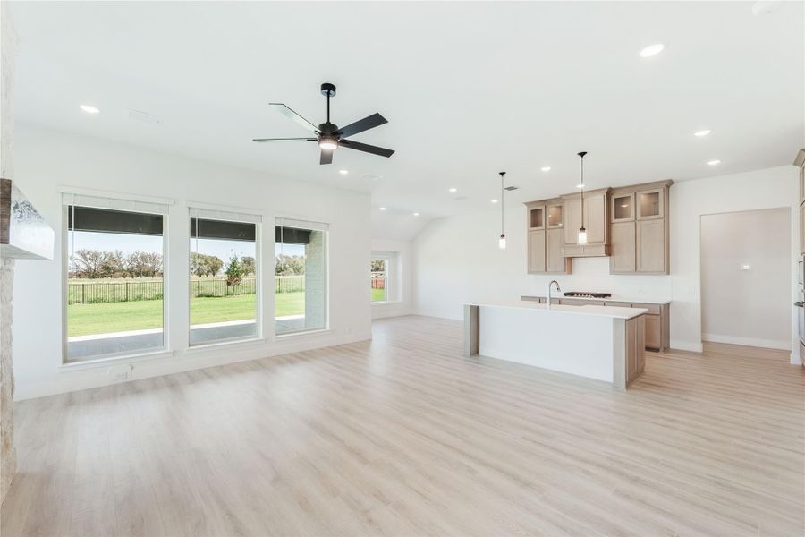 Open-concept living area with light wood floors, ceiling fan, and kitchen island with tan cabinets in background