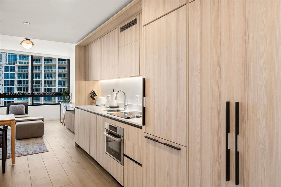 Kitchen featuring light wood-finish cabinetry, integrated appliances, matte black hardware, solid surface countertops, and floor-to-ceiling windows