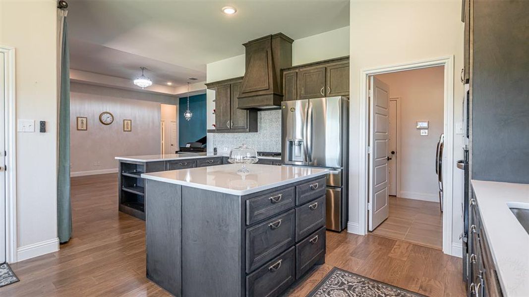 Open-concept kitchen featuring two islands with white countertops, dark wood cabinetry, stainless steel appliances, and wood-finish flooring