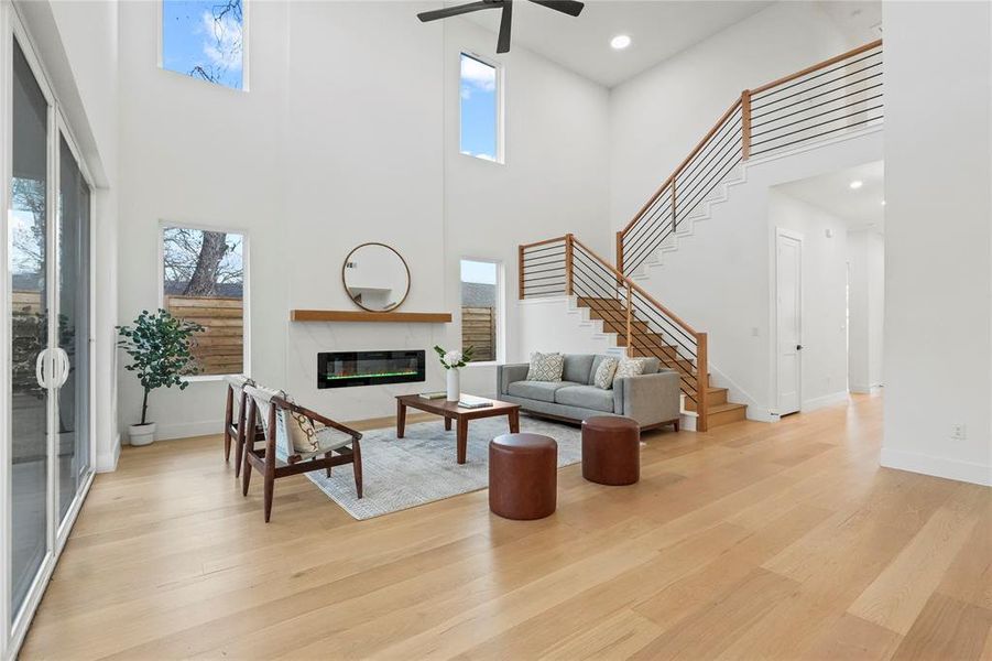 Living room with a fireplace, light wood-type flooring, a high ceiling, ceiling fan, and recessed lighting