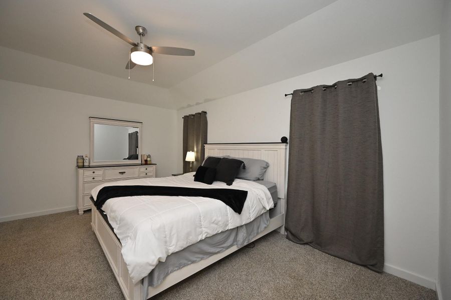 The primary bedroom features a modern design with neutral tones, a ceiling fan, and ample natural light through large windows. Carpeted flooring adds coziness and warmth. The primary bedroom features a modern design with neutral tones, a ceiling fan, and ample natural light through large windows. Carpeted flooring adds coziness and warmth.