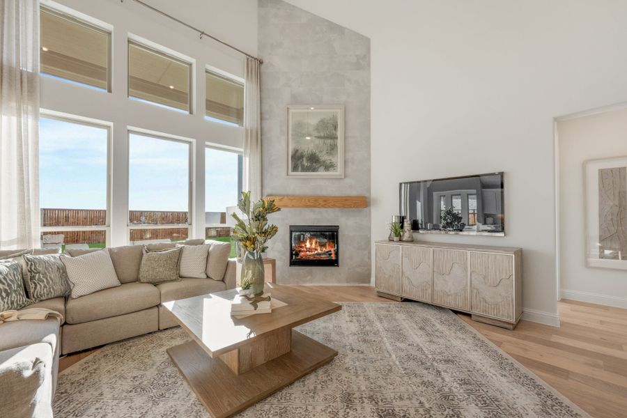 Living room with two-story windows, stone fireplace, hardwood floors, and neutral sectional sofa