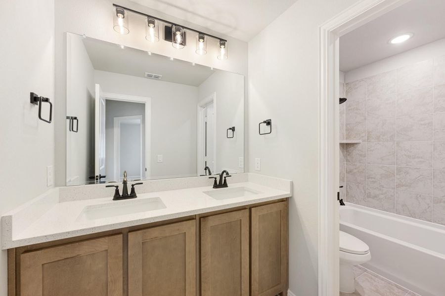 Bathroom with double sink vanity, wood cabinets, white countertop, and tiled shower-tub combo
