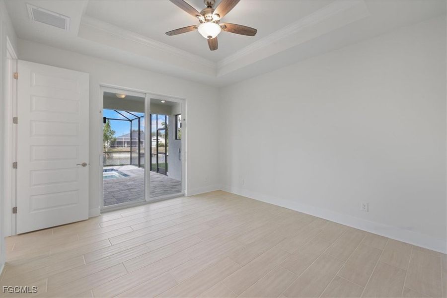 Empty room featuring a tray ceiling, a sunroom, wood tiled floors, a ceiling fan, and crown molding