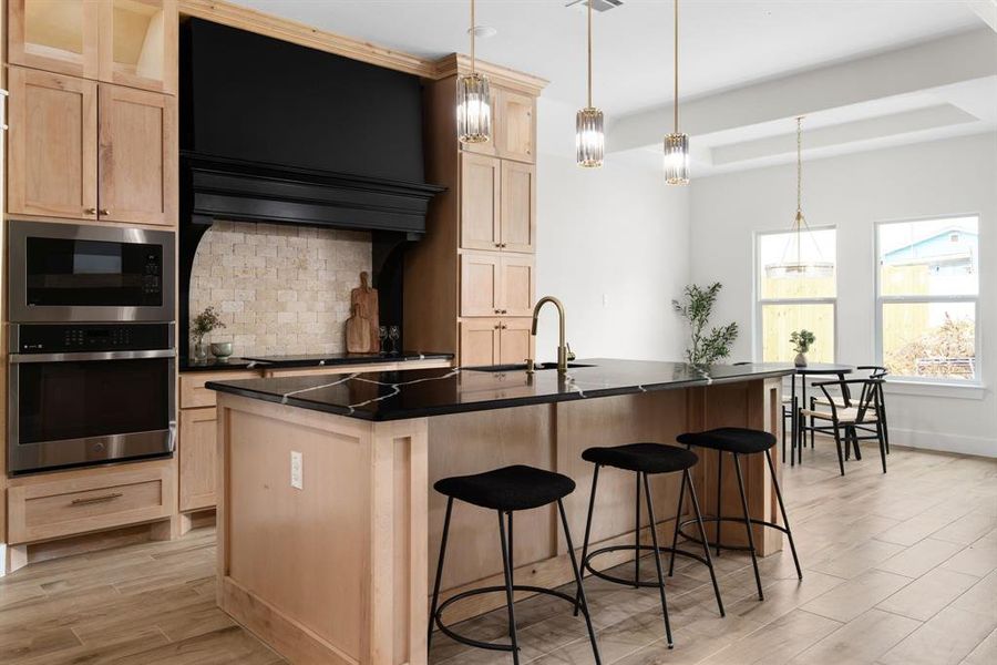 Kitchen with decorative light fixtures, a center island with sink, appliances with stainless steel finishes, sink, and decorative backsplash