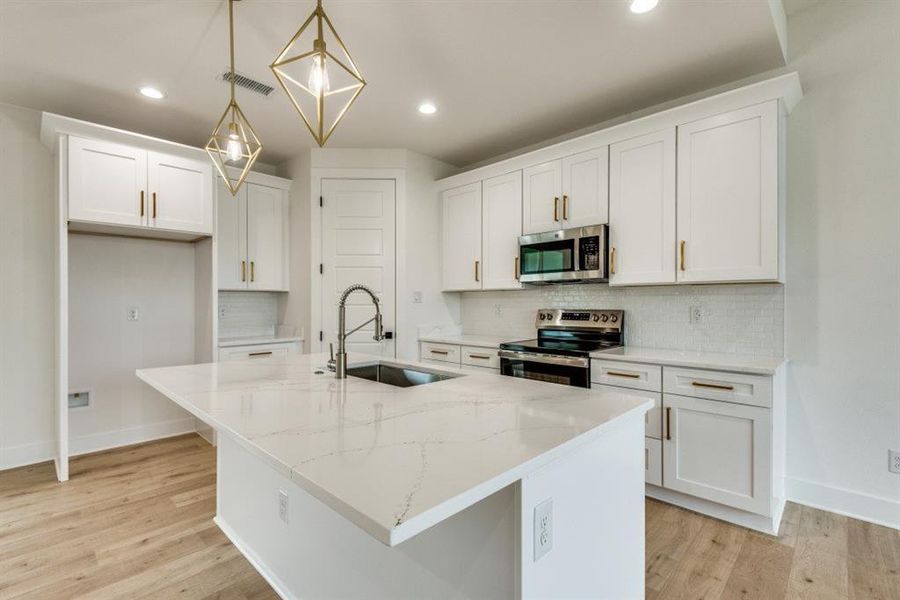 Kitchen featuring pendant lighting, a center island with sink, white cabinets, sink, and stainless steel appliances