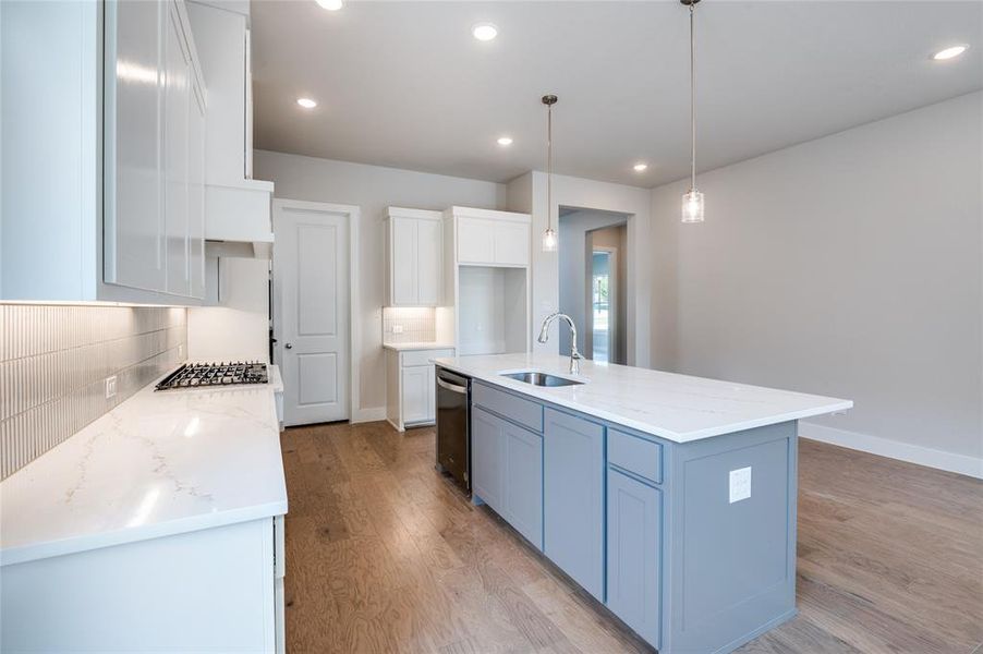 Kitchen with white cabinets, sink, light hardwood / wood-style flooring, and an island with sink