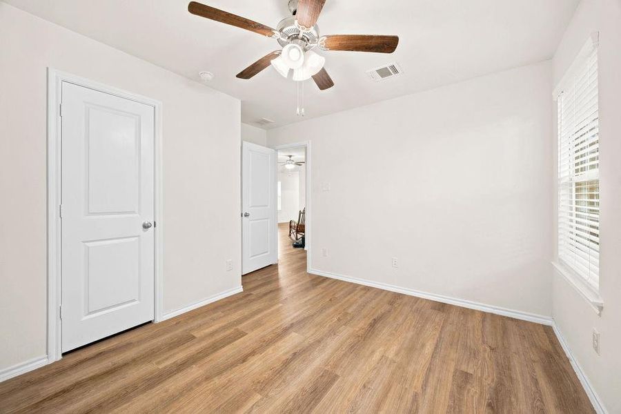 Room featuring wood-finish flooring, white walls, and a ceiling fan with wood-tone blades Room featuring wood-finish flooring, white walls, and a ceiling fan with wood-tone blades