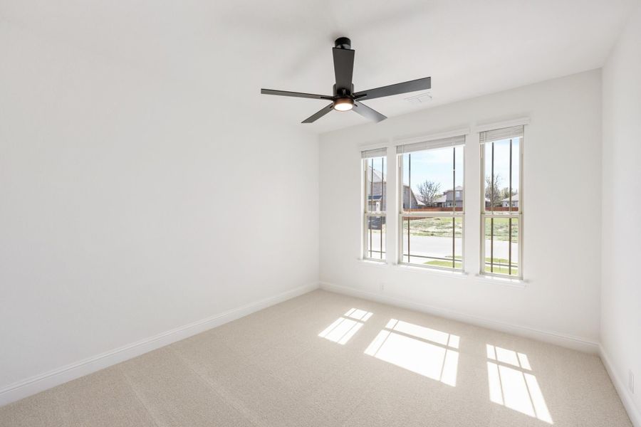 Empty bedroom with beige carpet, white walls, ceiling fan, and triple window with natural light
