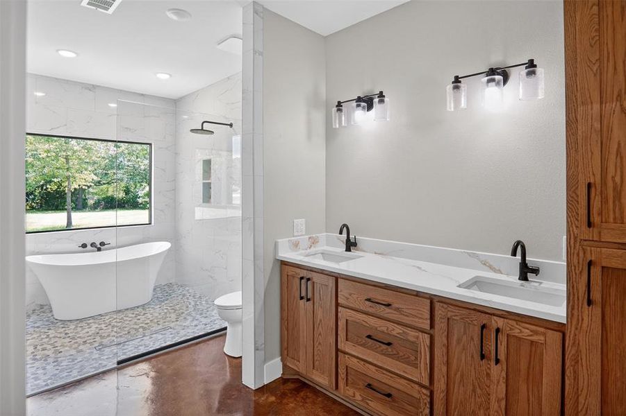 Primary Spacious bathroom featuring a dual vanity with wood cabinetry and light-toned countertops, matte black fixtures, an expansive freestanding tub, and a separate walk-in shower with pebble flooring Primary Spacious bathroom featuring a dual vanity with wood cabinetry and light-toned countertops, matte black fixtures, an expansive freestanding tub, and a separate walk-in shower with pebble flooring