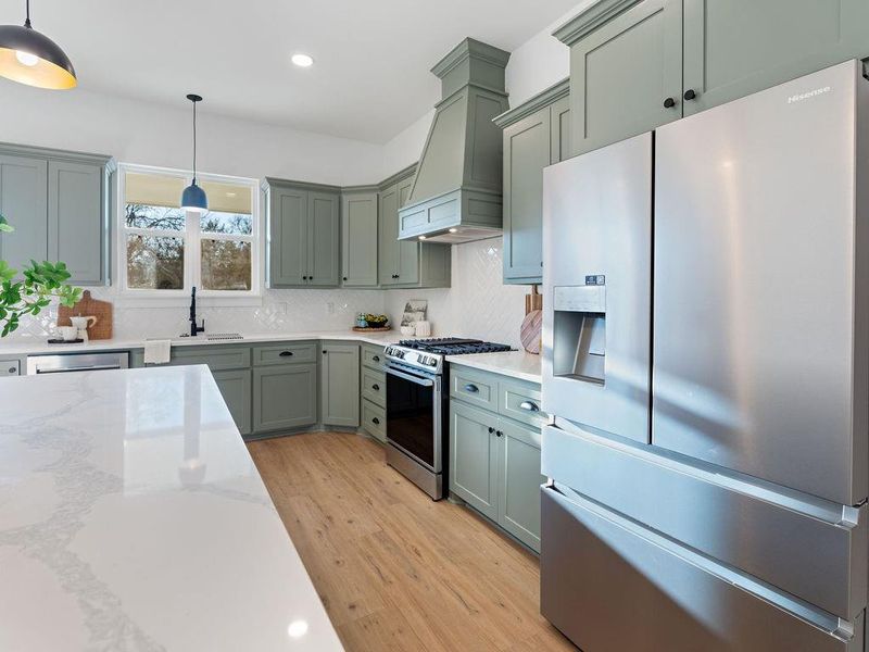Kitchen featuring stainless steel appliances, light wood-type flooring, pendant lighting, and light stone countertops