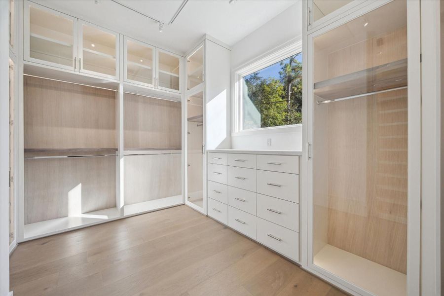 2/2 primary closet. Offers custom built-ins with ample hanging space, generous shelving, dedicated shoe storage,  sleek drawers, and glass enclosed casings.