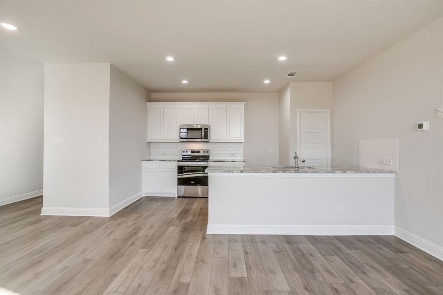 Kitchen with white cabinets, stainless steel appliances, a peninsula, light stone countertops, and recessed lighting