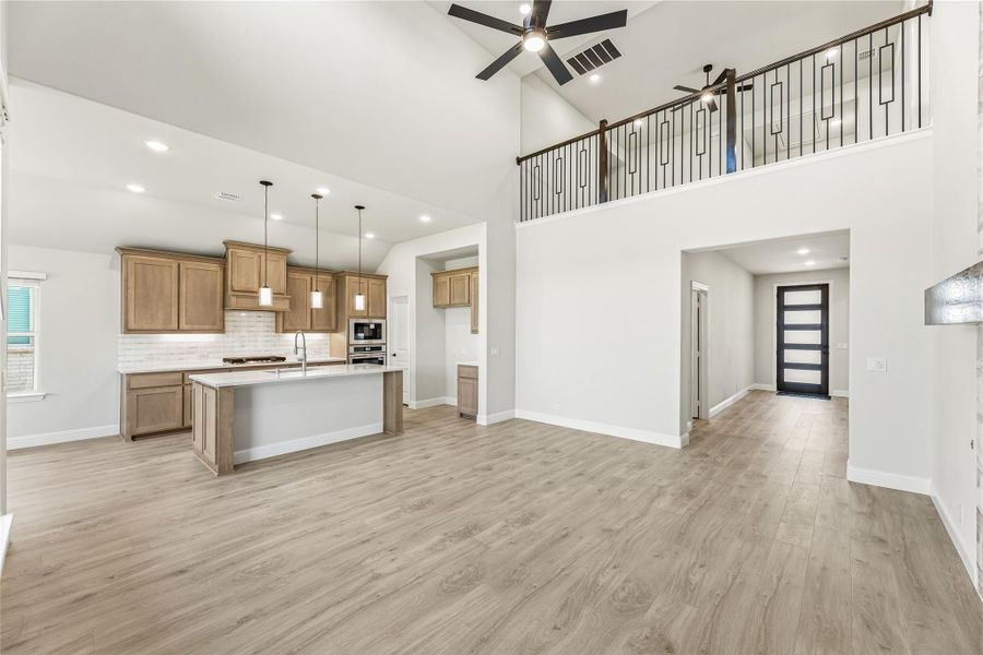 Open-concept living area with kitchen island, wood cabinets, high vaulted ceiling, and second-floor balcony railing.