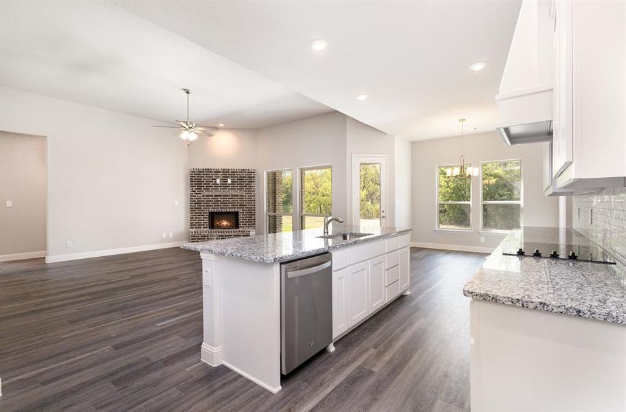 Kitchen with a brick fireplace, white cabinets, light stone counters, open floor plan, and recessed lighting Kitchen with a brick fireplace, white cabinets, light stone counters, open floor plan, and recessed lighting