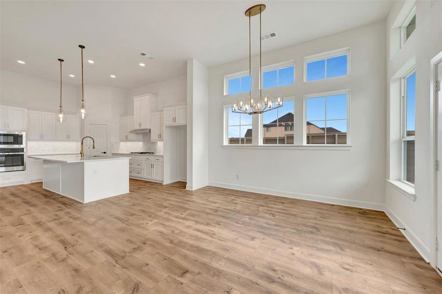 Open concept living space featuring wood-finish flooring, a kitchen island with seating, stainless steel appliances, a white tile backsplash, and multiple windows with transoms