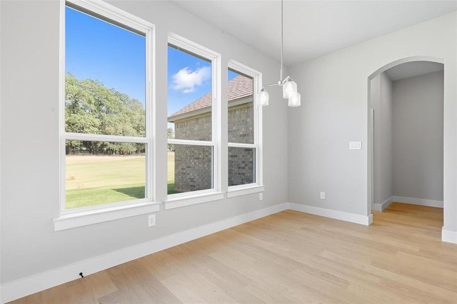 Unfurnished dining area with light wood-style floors, arched walkways, and a chandelier