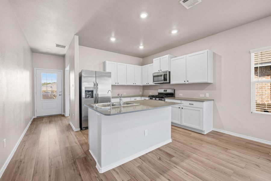 Kitchen featuring stainless steel appliances, white cabinets, a center island with sink, light wood-style floors, and recessed lighting