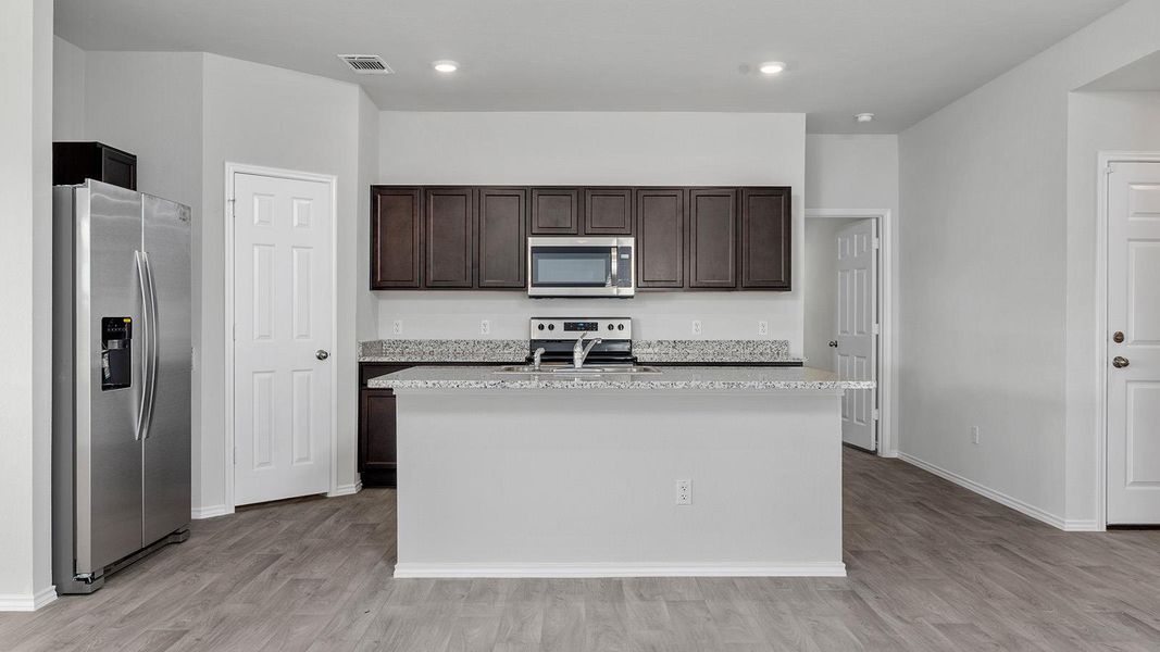Kitchen with stainless steel appliances, dark wood finish cabinets, light stone countertops, and light wood-style floors