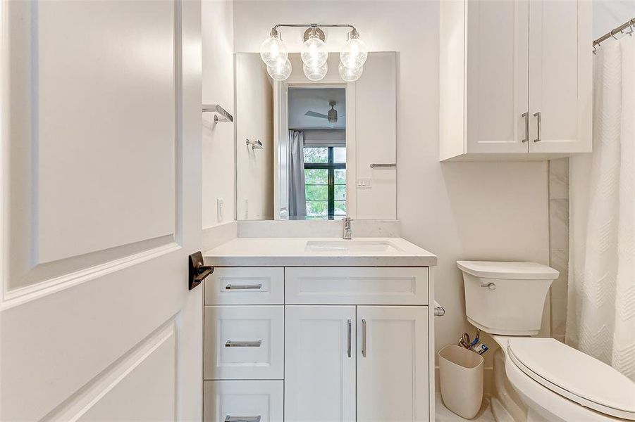 This bathroom features a sleek, modern design with white cabinetry and quartz countertops, a large mirror with elegant lighting, a standard toilet, and a tub and shower combination.