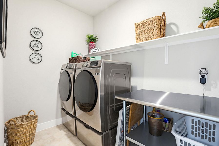 Dedicated laundry area featuring modern stainless steel appliances, a continuous wall-mounted shelf, and a stainless steel utility table