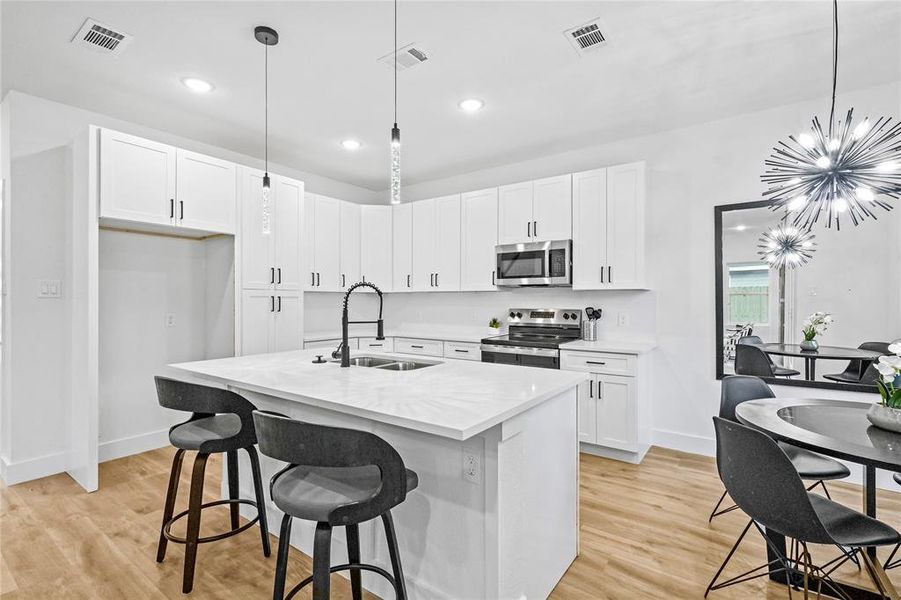 Kitchen with pendant lighting, a chandelier, an island with sink, and stainless steel appliances