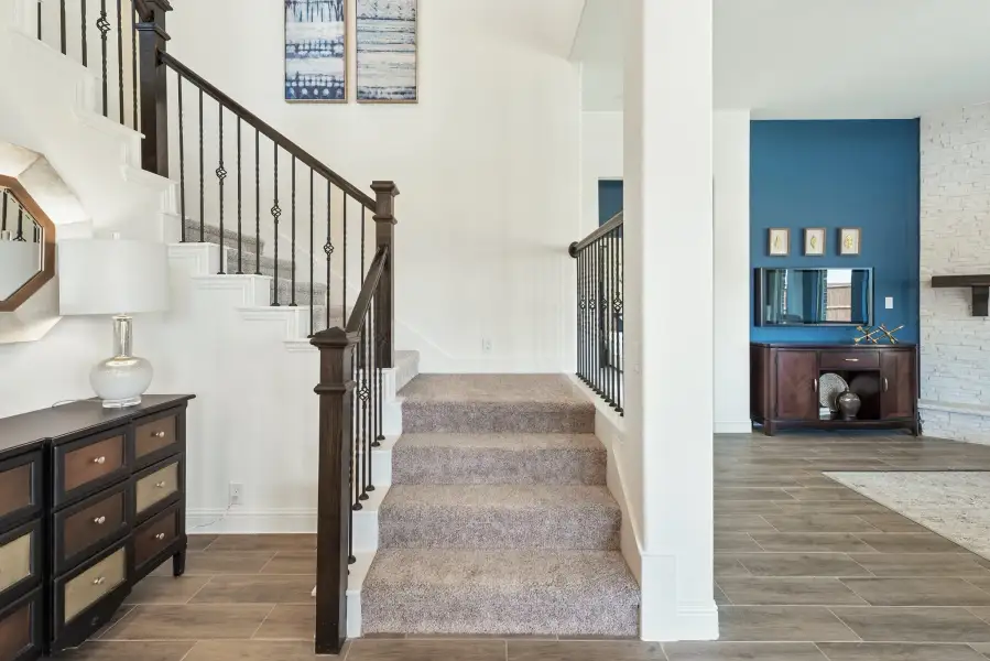 Carpeted staircase with dark wood and iron railing in an open foyer with tile floors and high ceilings