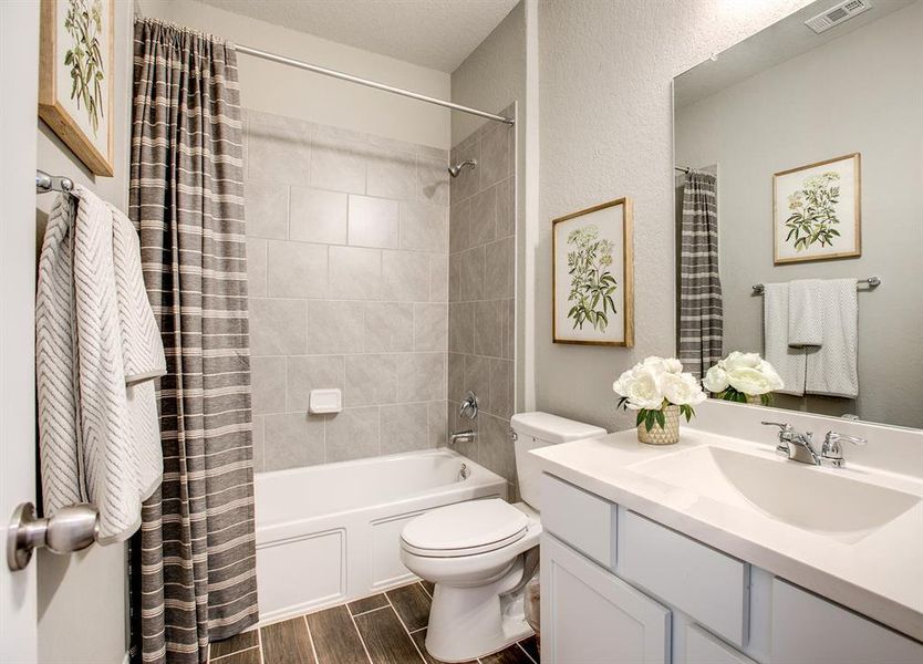 Full bathroom featuring vanity, shower / bath combination with curtain, wood finish floors, and a textured wall Full bathroom featuring vanity, shower / bath combination with curtain, wood finish floors, and a textured wall