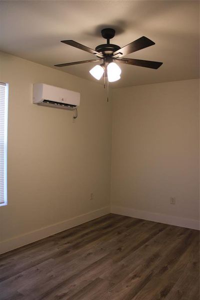 Unfurnished room featuring dark wood finished floors, ceiling fan, and a wall mounted AC