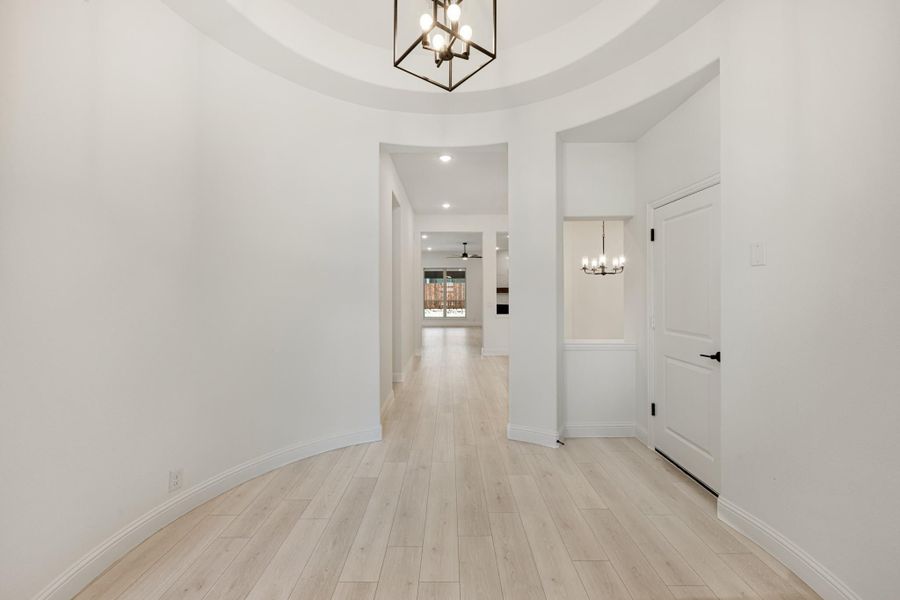 Circular entryway with tray ceiling, pendant chandelier, and light wood floors leading to open living area