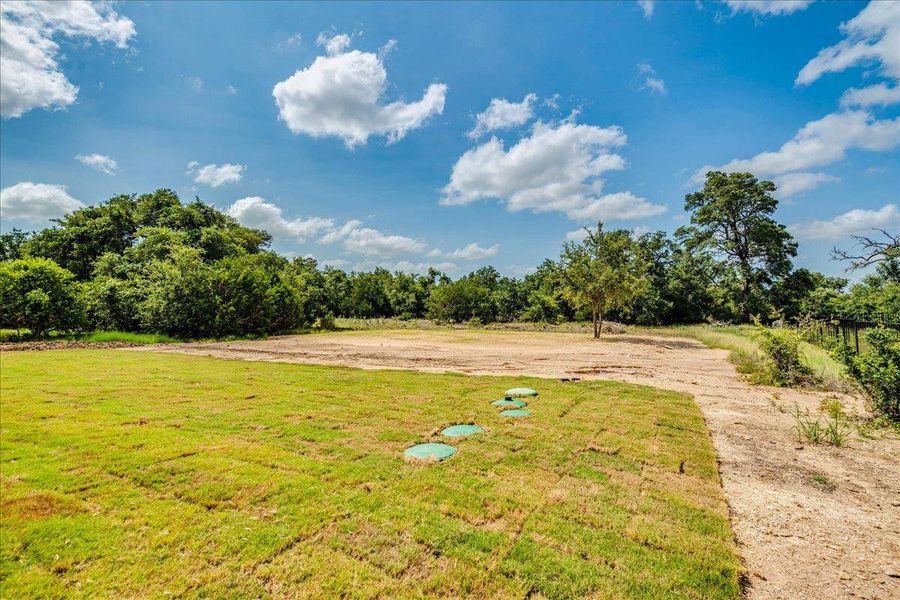 A spacious, verdant lot awaits your vision, bordered by a dense, natural treeline.