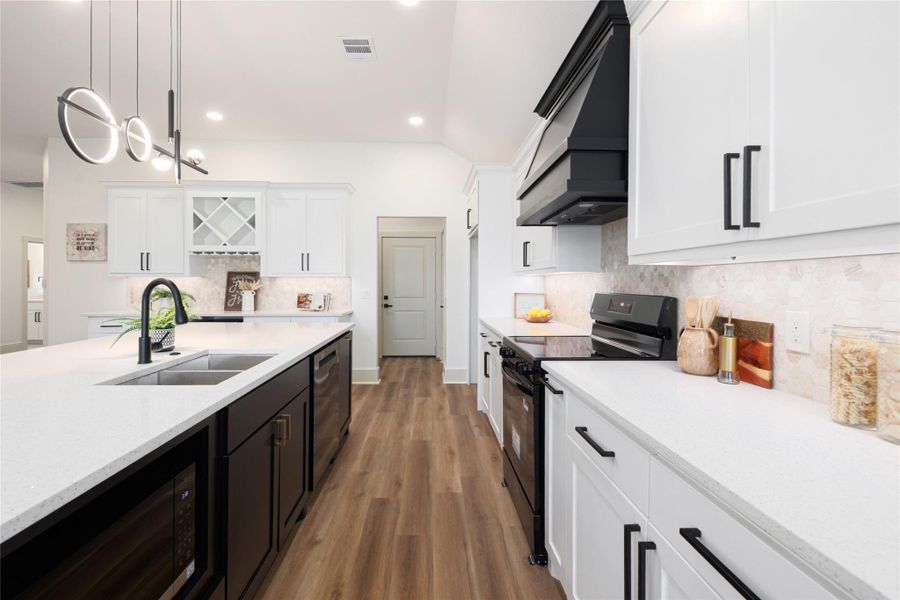 Kitchen featuring black appliances, backsplash, white cabinets, custom exhaust hood, and pendant lighting