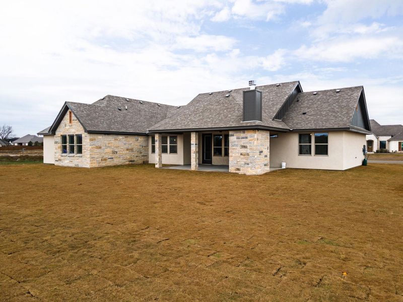 Rear view of house with stone siding, a patio area, and a lawn