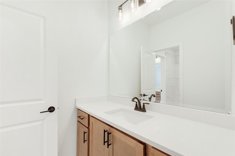 Bathroom vanity with wood cabinets, white quartz countertop, single sink, and large mirror with pendant lights above