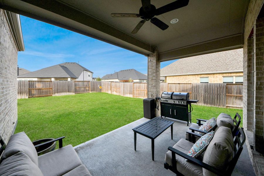 This photo shows a spacious covered patio with comfortable seating and a ceiling fan, overlooking a well-maintained fenced backyard. It features a grill, ideal for outdoor entertaining. This photo shows a spacious covered patio with comfortable seating and a ceiling fan, overlooking a well-maintained fenced backyard. It features a grill, ideal for outdoor entertaining.