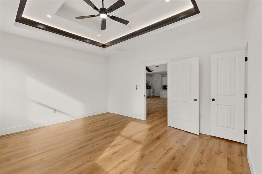 Unfurnished bedroom with a ceiling fan, light wood-style flooring, and a raised ceiling Unfurnished bedroom with a ceiling fan, light wood-style flooring, and a raised ceiling